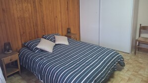 Ein Schlafzimmer mit einer Wandpaneele aus Holz, einem Bett mit gestreifter Bettw äsche, einem Nachttisch mit Lampe und einem Holzstuhl.