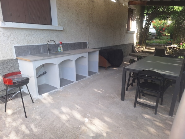An outdoor kitchen area with a barbecue grill, sink, and a table with chairs.