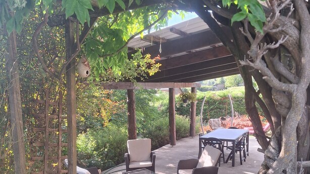 Ein Außenbereich mit Terrasse, Korbmöbeln, einer Pergola und einem gepflasterten Weg.