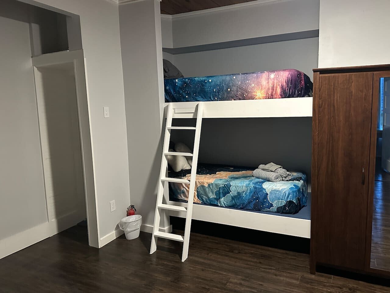 Ein Etagenbett mit Bettwäsche zum Thema Galaxie, eine weiße Leiter, ein Holzschrank und ein weißer Mülleimer.