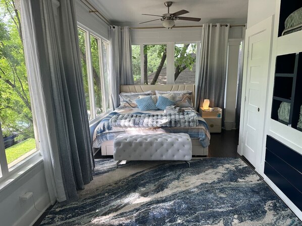 A bedroom with a bed, a ceiling fan, and a view of the outdoors.