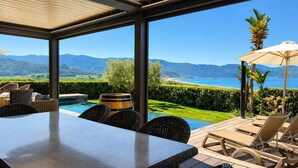 Un'area piscina con tavolo e sedie, vista sul mare e sulle montagne, e un pergolato.