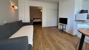 A modern, compact living space with a sofa, a bed, a TV, and a microwave.
