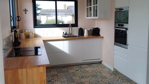 A kitchen with a window, white cabinets, a built-in oven, and a patterned floor. - Large, quiet house, large garden, heated swimming pool, ideal for families (La Baule-Escoublac)