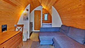A cozy attic bedroom with wooden walls, a bed, a sofa, and a small desk.