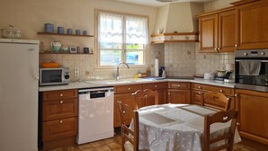 A kitchen with wooden cabinets, a white refrigerator, a microwave, a dishwasher, and a dining table with chairs. - La Parenthèse Verte, Guesthouse & Panorama (Mont-Saint-Jean)