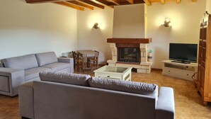 A living room with a sofa, a coffee table, a fireplace, a TV, and a dining table with chairs. - La Parenthèse Verte, Guesthouse & Panorama (Mont-Saint-Jean)