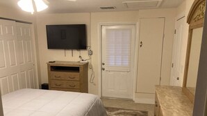 Quarto com cama, penteadeira, televisão e porta com janela.