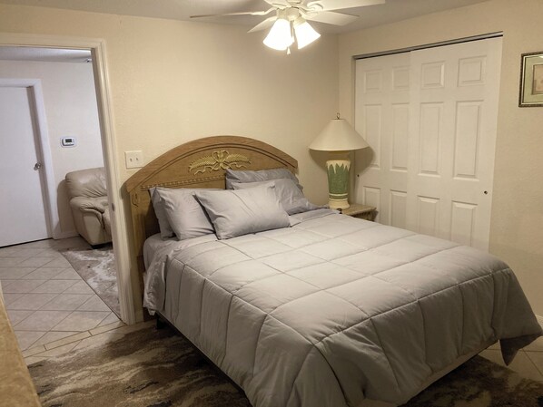 A bedroom with a bed, a chair, a lamp, and a ceiling fan.