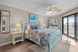 A bedroom with a bed, nightstands, a ceiling fan, a large window, and artwork on the walls.