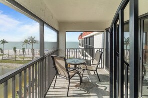 A balcony with a table and chairs, overlooking a beach and ocean.