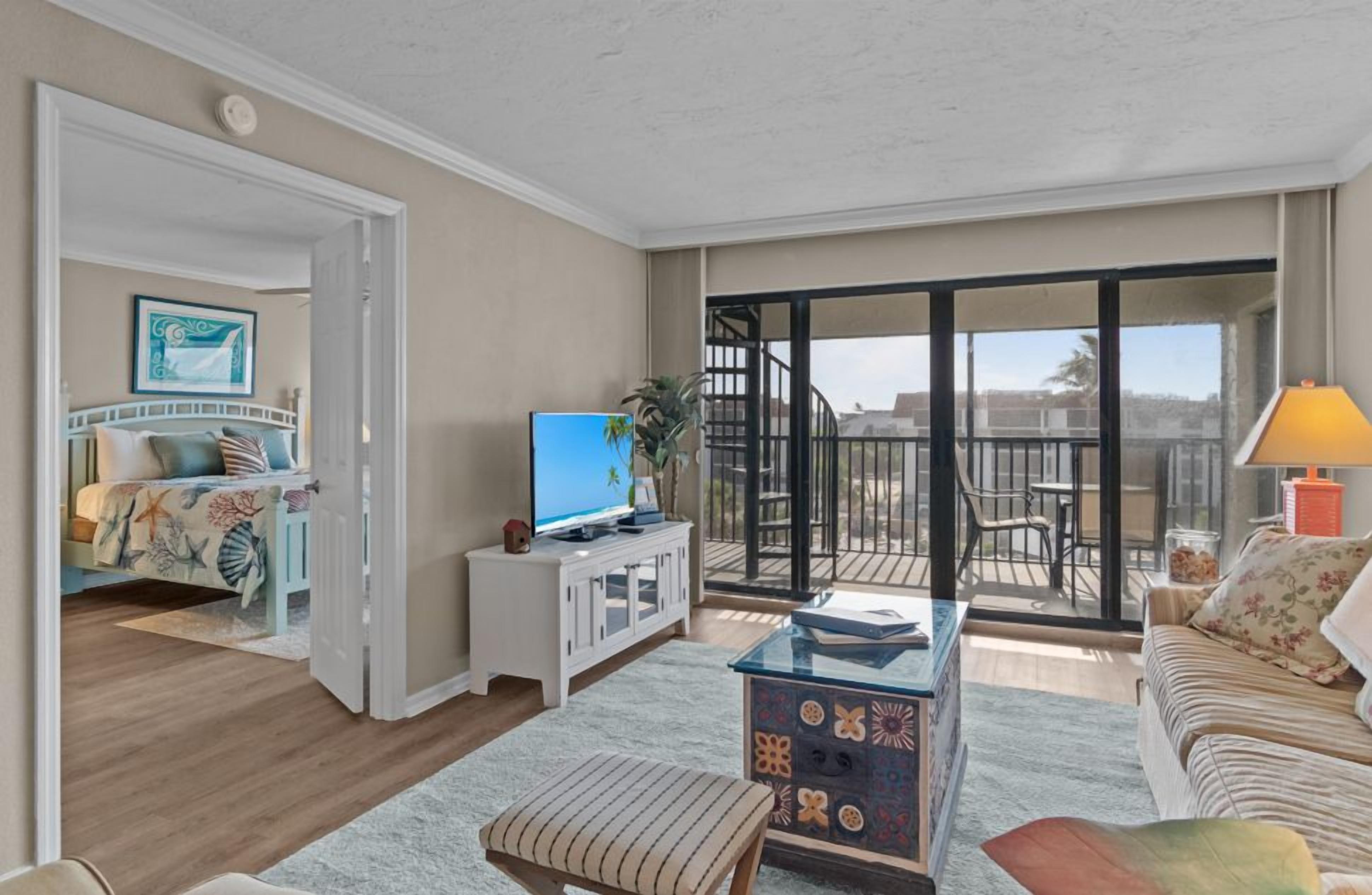 A living room with a TV, a sofa, a coffee table, and a balcony with a chair.