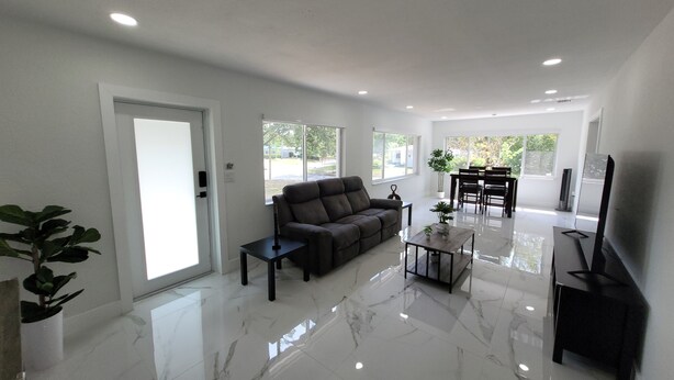 A modern living room with a sofa, coffee table, and TV, large windows, and a dining area. - 3-bedroom house in welcoming Temple Terrace, WiFi. EV car charging oulet, PS4 (Temple Terrace)