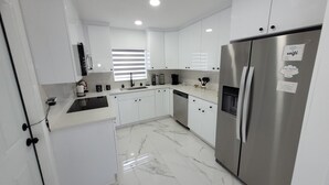 A modern kitchen with white cabinets, a stainless steel refrigerator, and a marble floor. - 3-bedroom house in welcoming Temple Terrace, WiFi. EV car charging oulet, PS4 (Temple Terrace)