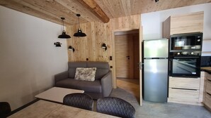 Un espacio habitable compacto con sofá, mesa de comedor y cocina equipada con refrigerador y horno.