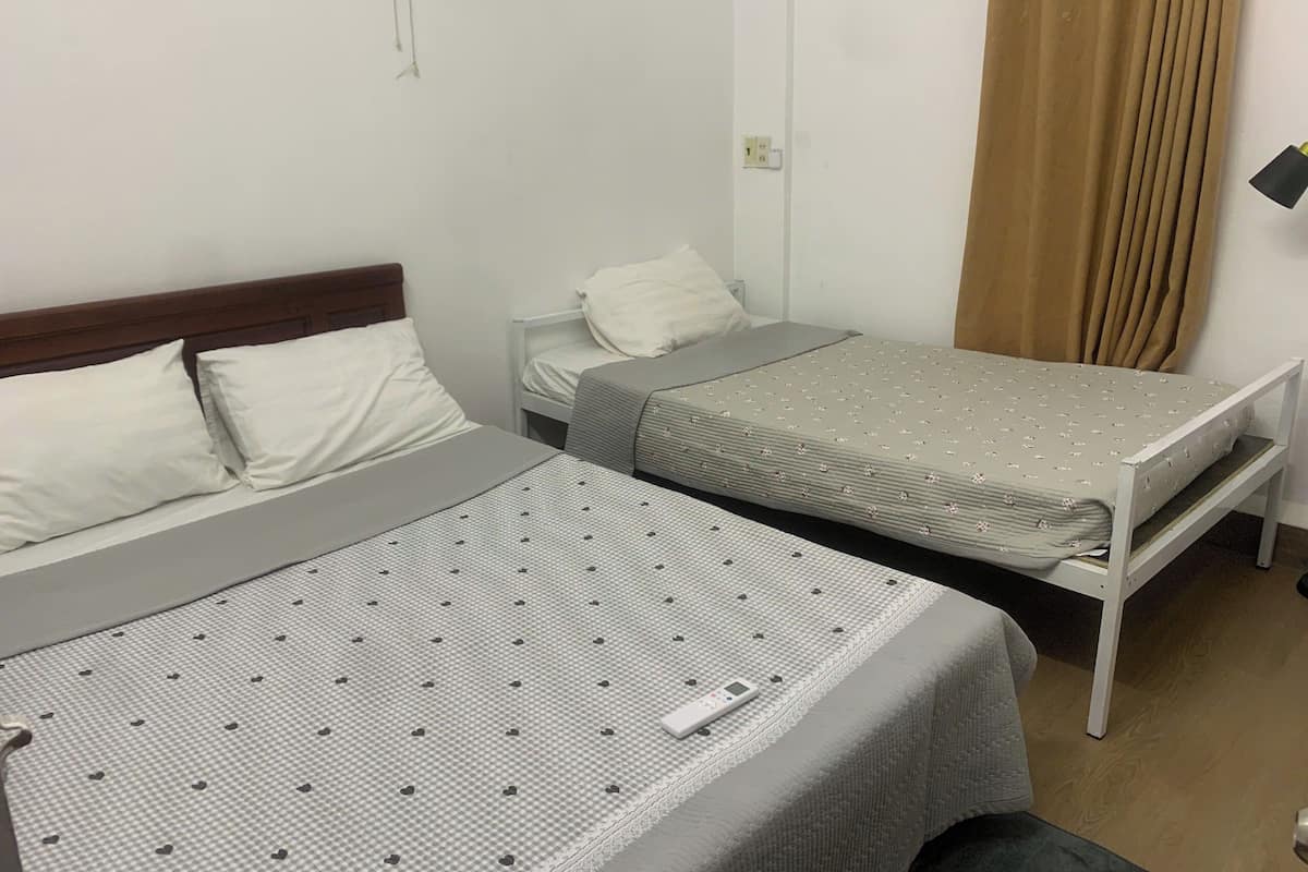 Ein Zimmer mit zwei Betten, jedes mit einer anderen Bettdecke. Am rechten Bettende steht ein Nachttisch mit einer Lampe.