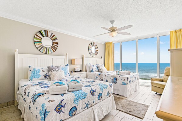 A bedroom with two beds, a ceiling fan, large windows with a view of the ocean, and decorative wall mirrors. - Sunset Hideaway! 3BR 3BA Sleeps 10! Beachfront! Seasonal Beach Chairs! (Panama City Beach)
