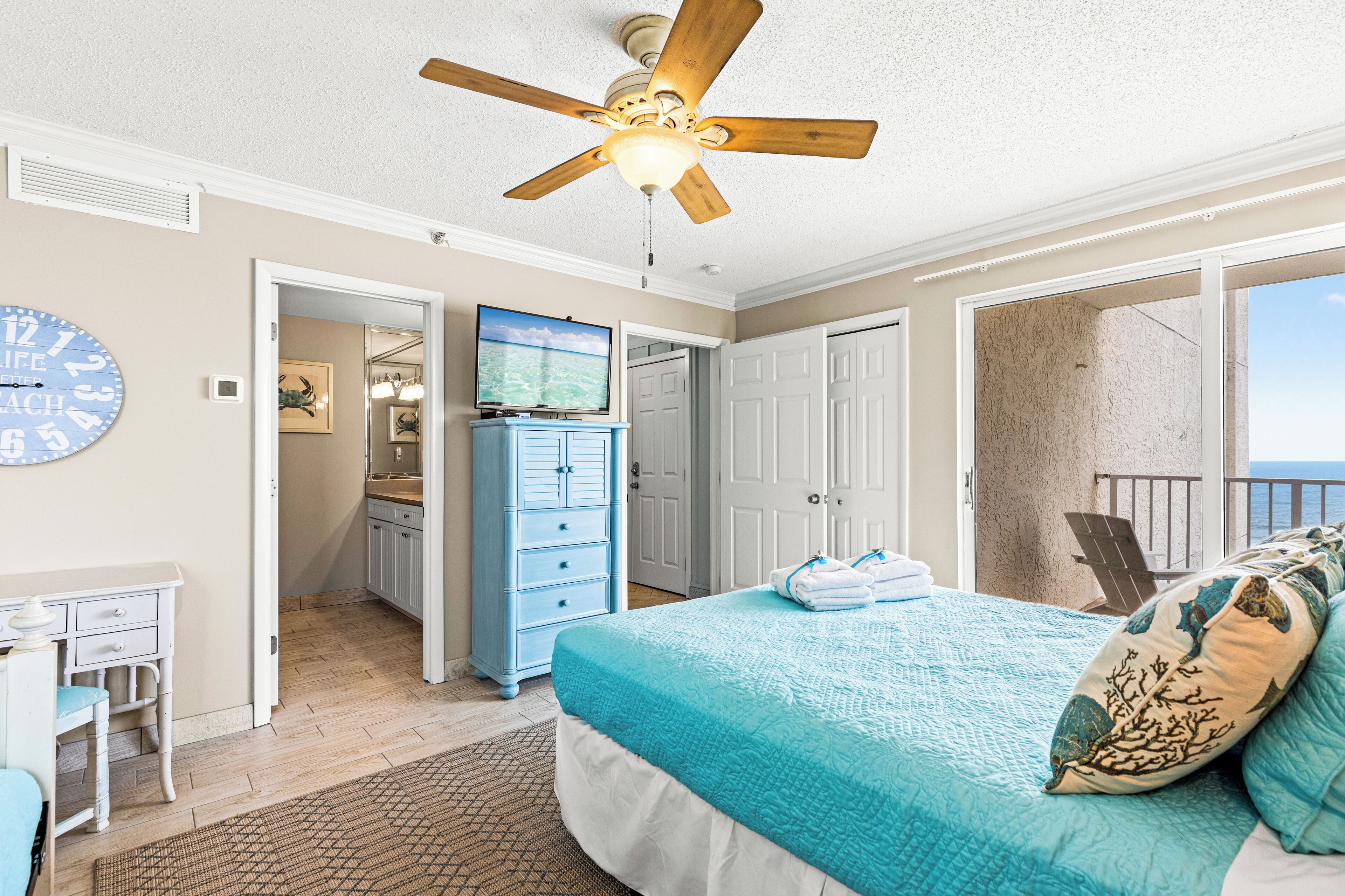 Une chambre à coucher avec un lit, un ventilateur de plafond, une horloge, une commode et une vue sur l’extérieur.