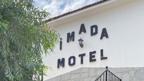 A sign for 'IMADA MOTEL' with a stone wall and a staircase leading up. - İMADA MOTEL  (Ayvacik)