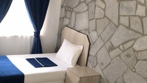 A hotel room with a stone wall, a bed with a blue bedspread, a bedside table, and an air conditioning unit. - İMADA MOTEL  (Ayvacik)
