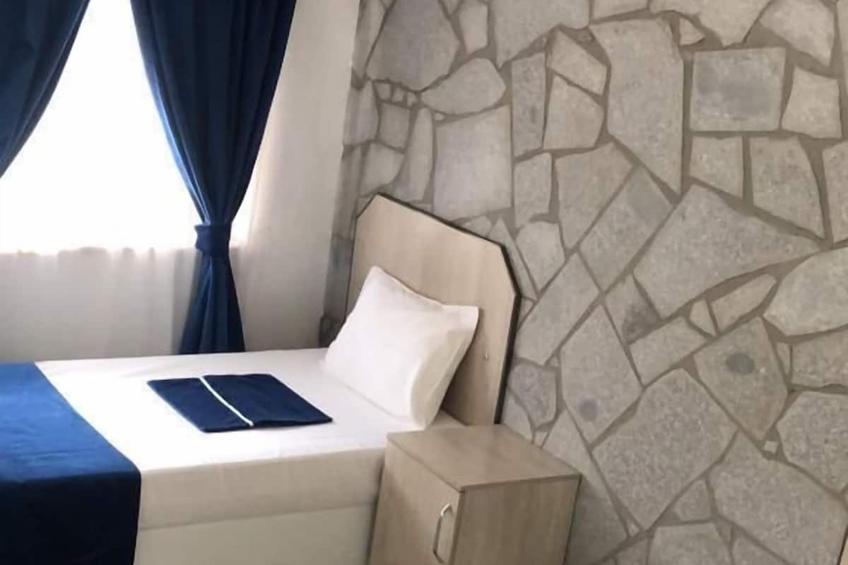 A hotel room with a stone wall, a bed with a blue bedspread, a bedside table, and an air conditioning unit.