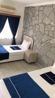Quarto de hotel com parede de pedra, cama com colcha azul, mesa de cabeceira e aparelho de ar condicionado.