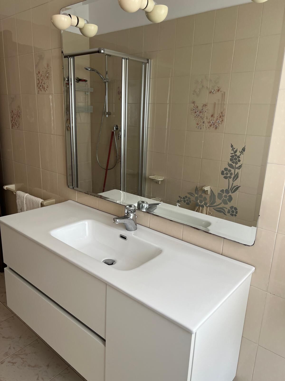 Un baño con un lavabo blanco, un espejo y una cabina de ducha.