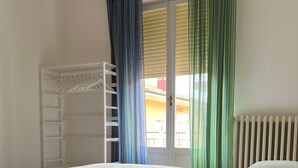 A bedroom with a bunk bed, a window with curtains, a radiator, and a chair.