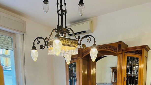 A living room with a sofa, a glass-top coffee table, a wooden cabinet with glass doors, and a chandelier.