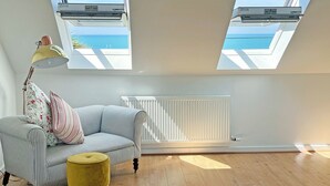 A room with a striped sofa, a yellow ottoman, and a radiator. There are two skylights with views of the sea. - 2 bedroom accommodation in Seaford (Seaford)
