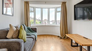A modern living room with a grey sofa, a wooden coffee table, and a large window with curtains. - 2 bedroom accommodation in Seaford (Seaford)