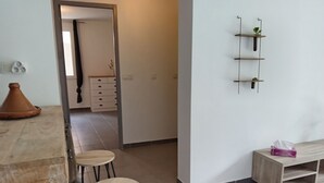 A modern kitchen with a wooden countertop, two stools, a cabinet, and a wall-mounted shelf with plants. - Loue Grand F3 climatisé Haute Corse, 2 grandes chambres (Furiani)