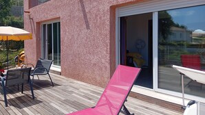 A balcony with a wooden deck, a pink sun lounger, and a yellow umbrella. - Loue Grand F3 climatisé Haute Corse, 2 grandes chambres (Furiani)