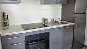 A modern kitchen with grey cabinets, a stainless steel sink, and a built-in oven. - Loue Grand F3 climatisé Haute Corse, 2 grandes chambres (Furiani)