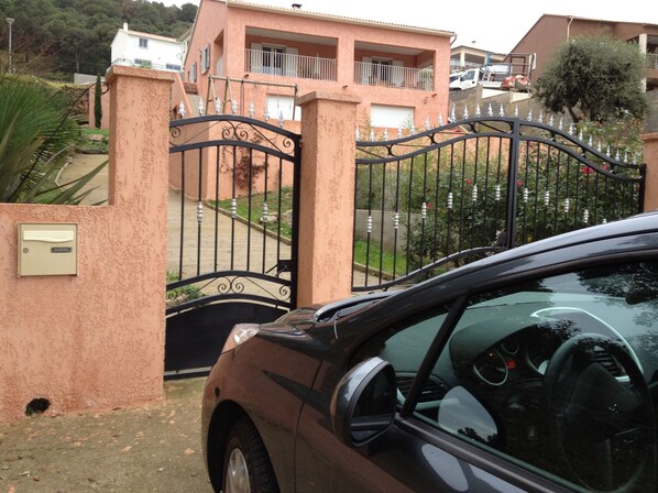A car parked in front of a gated entrance with a metal gate and a small mailbox on the wall. - Loue Grand F3 climatisé Haute Corse, 2 grandes chambres (Furiani)