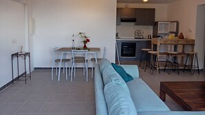 A modern living room with a sofa, a dining table with chairs, and a kitchen area with a stove and cabinets. - Loue Grand F3 climatisé Haute Corse, 2 grandes chambres (Furiani)