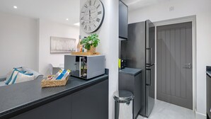 A modern kitchen with a large wall clock, a built-in oven, and a grey door. - Newly Converted 2BDR 1BA APT in Hounslow (Hounslow)