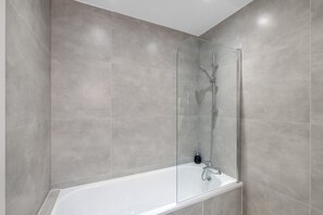 A modern shower enclosure with a glass door, a handheld showerhead, and a handheld showerhead with a spray attachment. - Newly Converted 2BDR 1BA APT in Hounslow (Hounslow)