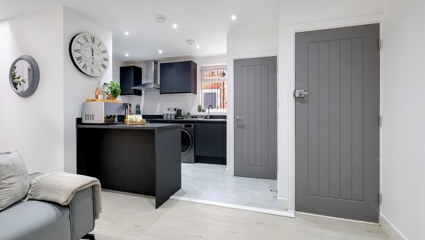 A modern kitchen with a central island, a grey door, and a grey sofa in a living area. - Newly Converted 2BDR 1BA APT in Hounslow (Hounslow)