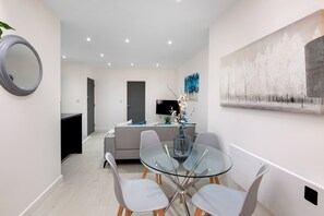 A modern living room with a glass dining table, white chairs, a grey sofa, a flat-screen TV, and a large abstract painting on the wall. - Newly Converted 2BDR 1BA APT in Hounslow (Hounslow)