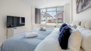 A modern hotel room with a large bed, a flat-screen TV, a window with blinds, and a painting on the wall. - Newly Converted 2BDR 1BA APT in Hounslow (Hounslow)