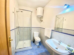 Un baño con cabina de ducha de vidrio, inodoro, lavamanos y espejo.