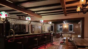 A bar area with a long counter, multiple stools, and a large mirror. - Bulk-Haus (Seesen)