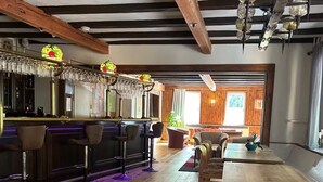 A bar area with wooden floors, bar stools, and a bar counter. There are hanging lights and a large window in the background. - Bulk-Haus (Seesen)