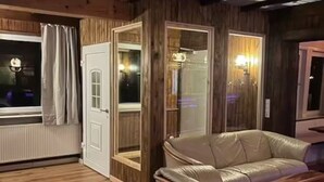 A cozy room with a wooden ceiling, a white leather sofa, and a large window with curtains. - Bulk-Haus (Seesen)