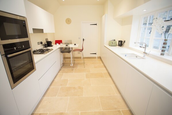 A modern kitchen with white cabinets, a stove, and a sink. - Craigmoor Cottage, central & tranquil, Bourton-on-the-Water, Cotswolds (Bourton-on-the-Water)