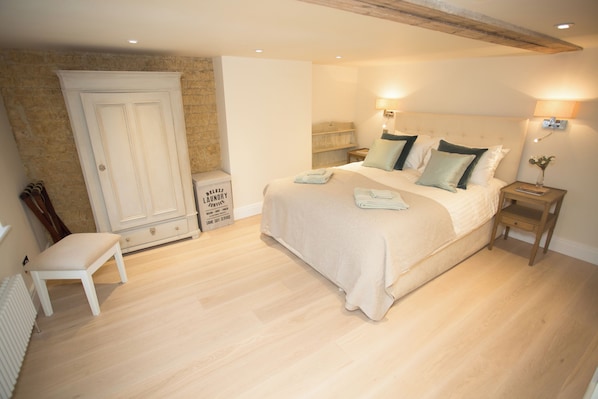A bedroom with a large bed, a wardrobe, a bench, and a radiator. - Craigmoor Cottage, enchanting, tranquil & central in Bourton-on-the-Water (Bourton-on-the-Water)
