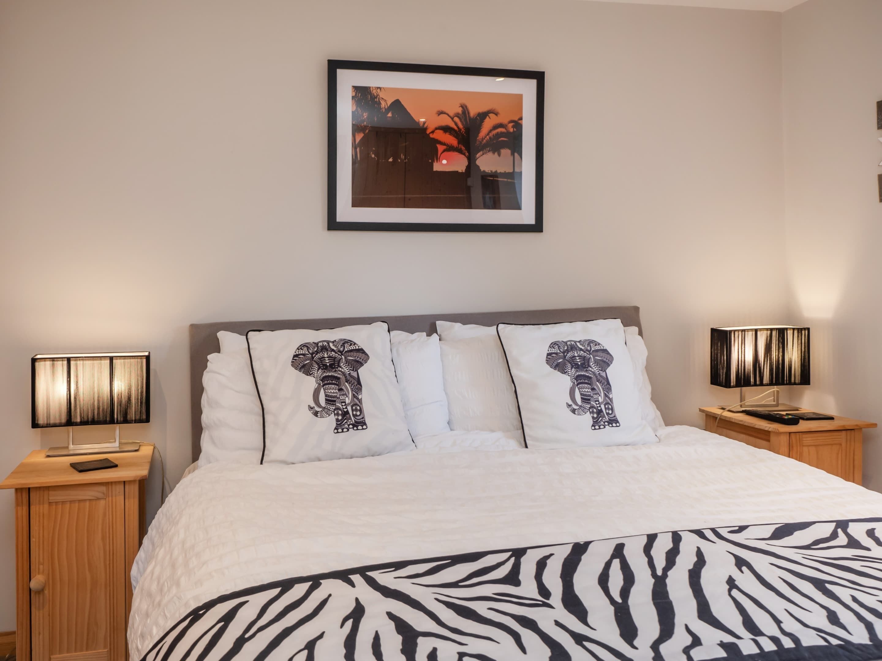 A bed with a zebra-patterned bedspread, two bedside lamps, and a framed picture on the wall.