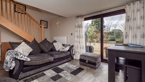 A modern living room with a sofa, ottoman, and a desk. A staircase is visible in the background. - Cottage in Norfolk Near River Yare (Norwich)