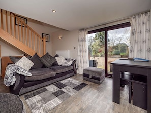 A modern living room with a sofa, ottoman, and a desk. A staircase is visible in the background. - Cottage in Norfolk Near River Yare (Norwich)
